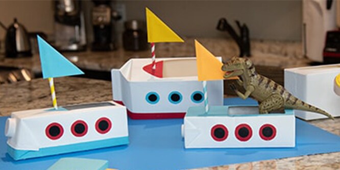 Paper boats with little flags on a blue sheet of construction paper.
