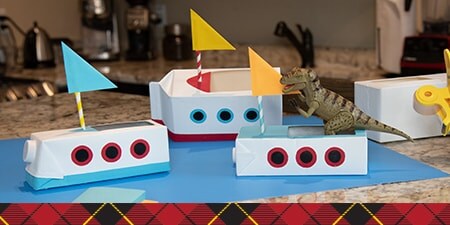 Paper boats with little flags on a blue sheet of construction paper.
