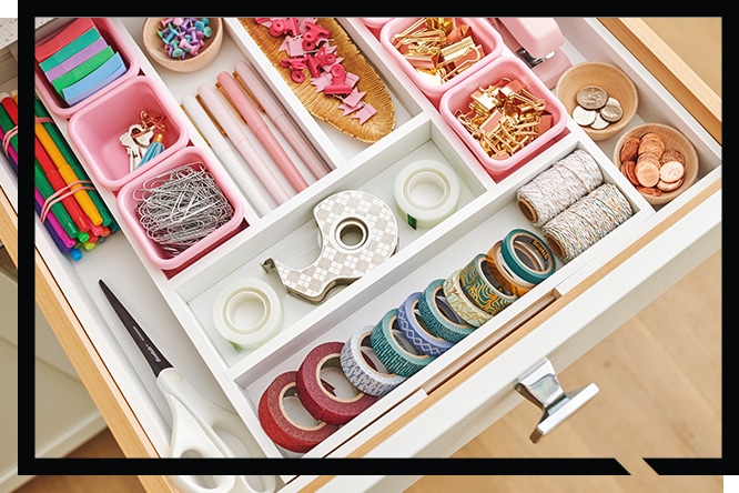 Organized drawer with stationery supplies, tape, twine, clips, washi tapes, scissors, and coins in compartments.
