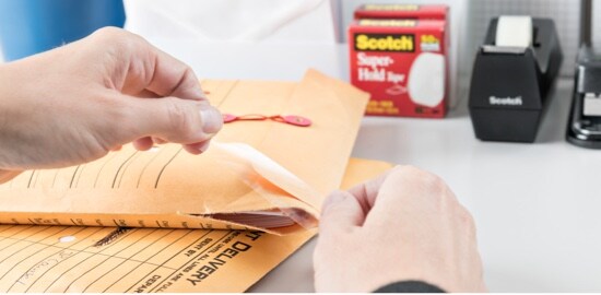 A ripped brown interoffice envelope being mended with Scotch® Super-Hold Tape.
