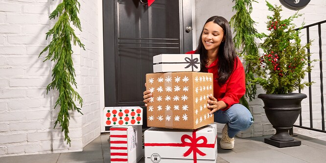 A person crouched next to a pile of gifts in boxes by an entryway door.
