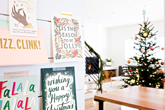 Christmas cards displayed on a wall with a decorated tree in the background.
