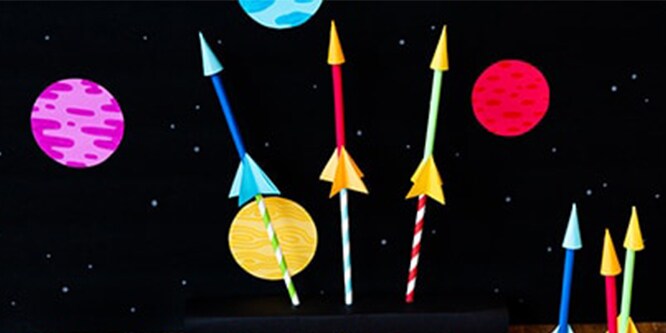 A black starry night background with paper straws that create DIY rockets.
