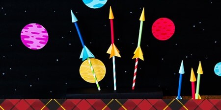 A black starry night background with paper straws that create DIY rockets.
