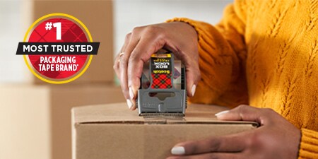 a person using Scotch® Box Lock™ tape to seal a cardboard box.
