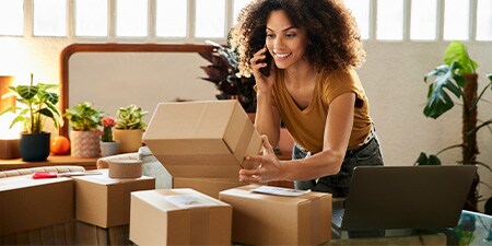 A woman on the phone next to a pile of shipping boxes.
