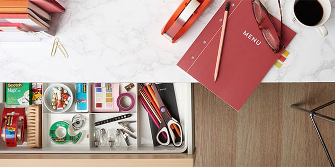 A desk with a drawer open showing various stationary.
