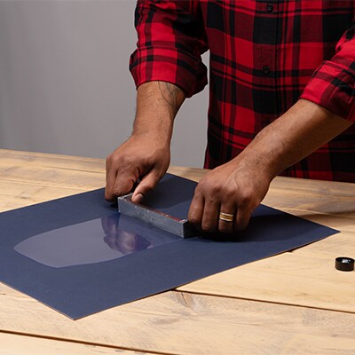 A person wearing a red plaid shirt applying adhesive to a surface.