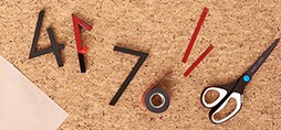 Numbers being taped, next to scissors, gloves, and other tools on a cork board.