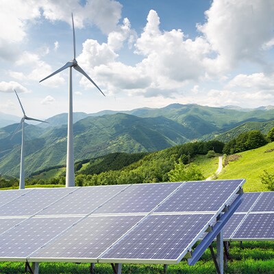 A mountainous landscape with windmills and solar panels in the foreground.