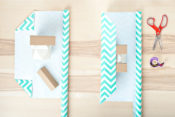 Gift wrapping tutorial showing two stages of wrapping a box with chevron-patterned paper, with red scissors and tape on a wooden surface.
