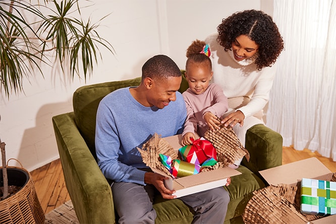 Family opening holiday gifts together on a green sofa, smiling and enjoying the moment.
