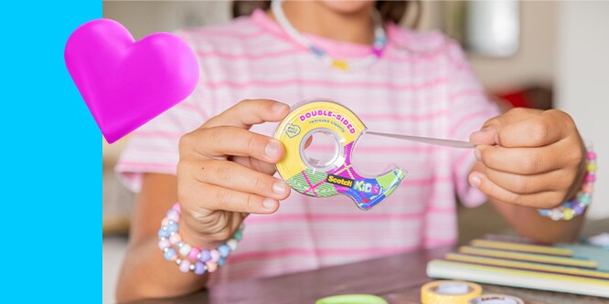 a girl in a pink striped shirt pulls tape from a Scotch® Double-Sided Kids Tape dispenser. Pink emoji heart in the top right corner.
