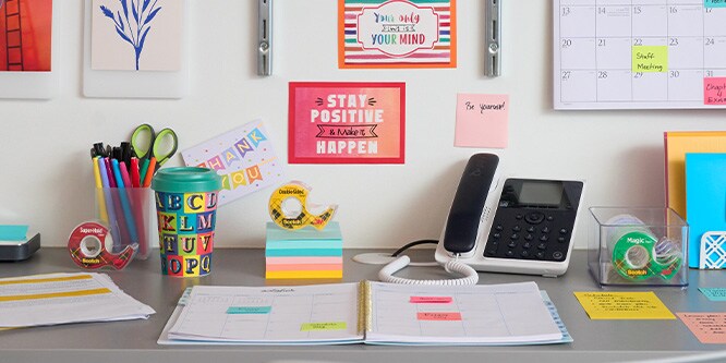 A colorful organized desk with post-it notes, scotch tape, a planner, pens, and a phone.
