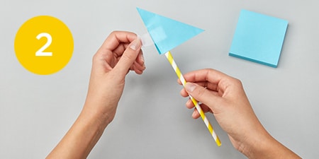 person taping a folded post-it® note to a straw
