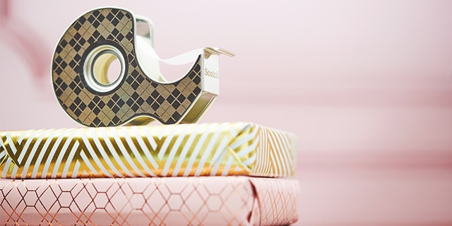 The Scotch® Stainless Steel Tape Dispenser on top of a pile of wrapped gifts in front of a pink background.