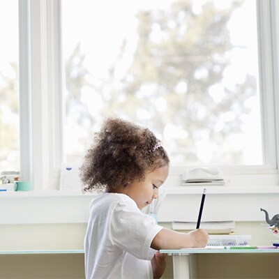 A young child drawing in front of a window.