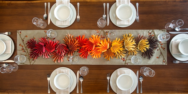 A table set with plates and silverware with DIY paper decor in the middle resembling fall leaves.