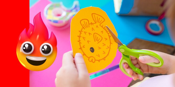 A kid cutting out a drawing of a pufferfish on orange paper using Scotch™ Kids Scissors. A Fire emoji face on the left side of the image.
