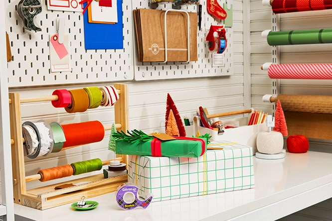 Gift wrapping station with assorted ribbons, paper, and tools on a white counter with organized wall displays.
