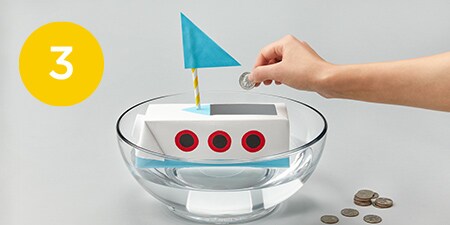 person putting a coin into a crafted boat in a bowl of water
