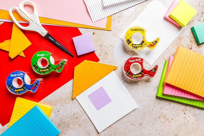 Craft supplies, including scissors, tape rolls, colored paper, and sticky notes, are arranged on a textured surface.

