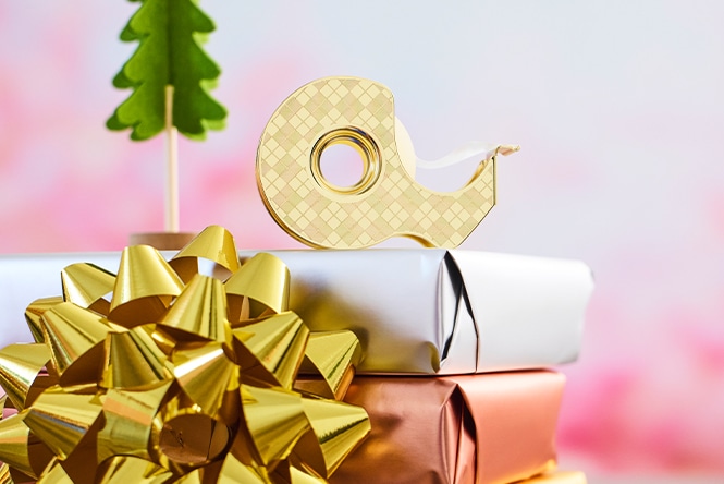 Gift-wrapped presents with a gold bow, decorative tape, and small tree adorn a festive scene.
