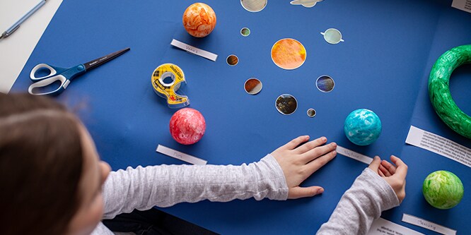 A table with a person making DIY solar system crafts using Scotch® Double-Sided Tape.
