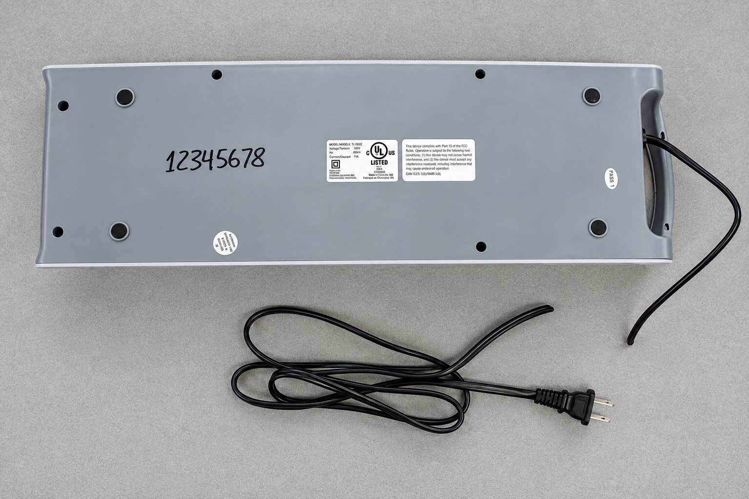 Gray electronic device with model and compliance labels, serial number 12345678, and a detached power cord on a gray background.
