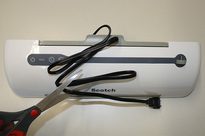 Scissors cutting the cord on the Scotch TL909-50 Laminator.
